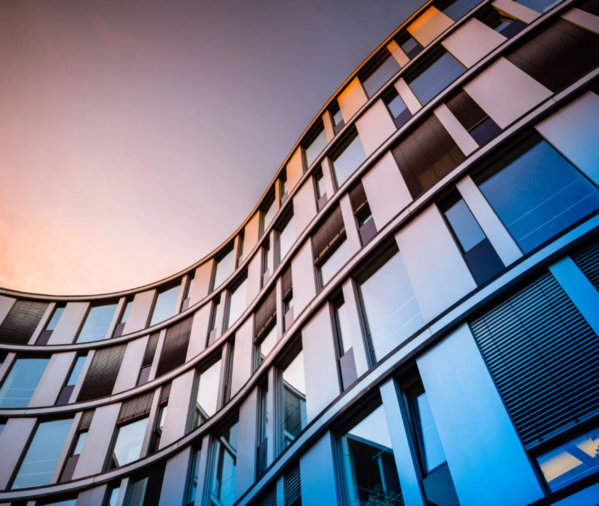 Modern curved glass building against sunset sky.